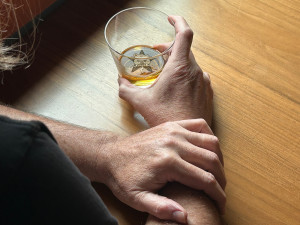 The hands & glass of whiskey of a deadbeat day-drinking - with the Self Help Radio logo floating in the glass.