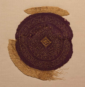 A circular fragment of purple wool is adorned with gold foil and pale silk stitching which displays three overlapping squares