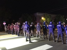 Approximately fifteen Oregon State Troopers stand in a riot line on Denver St in Kenton, Portland