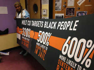 Teressa Raiford on Don't Shoot Portland's 10th anniversary march on MLK Day Teressa Raiford holds banner listing Black incarceration rates in Multnomah County