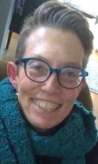 Smiling white woman with short gray hair, blue glasses, and a blue scarf