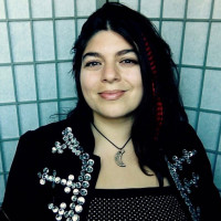 A Latina woman with long hair and a red feather in her hair.